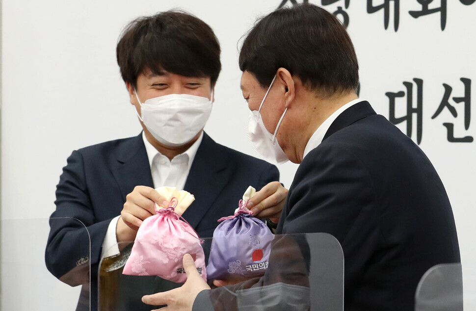 People Power Party leader Lee Jun-seok gives the party’s presidential nominee Yoon Seok-youl two silk bags while at a party Supreme Council meeting held at the National Assembly in Seoul’s Yeouido on Monday. (pool photo)