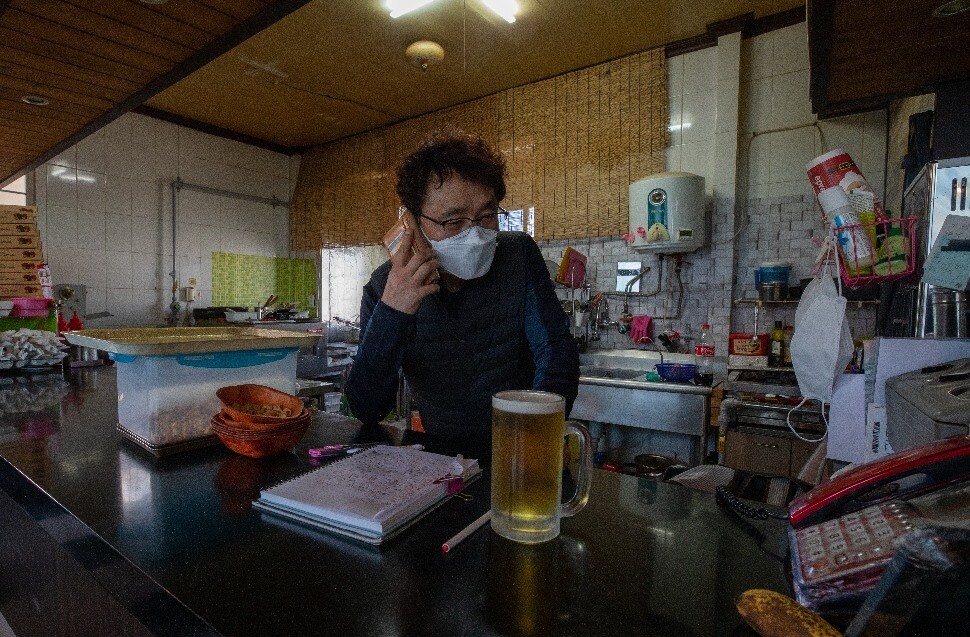 동네 치킨집 사장님이 휴대전화로 배달 주문을 받고 있다. 배달 갈 때마다 필요한 마스크 여러 개를 선반에 걸어놓았다.