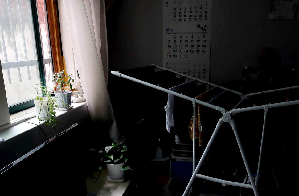 Clothes soaked during the flooding hang to dry in the living room of a semi-basement apartment in Seoul’s Seongbuk District on Aug. 16. Despite it being the middle of the afternoon, the room remains dark due to a wall around the building the apartment is located in. (Baek So-ah/The Hankyoreh)