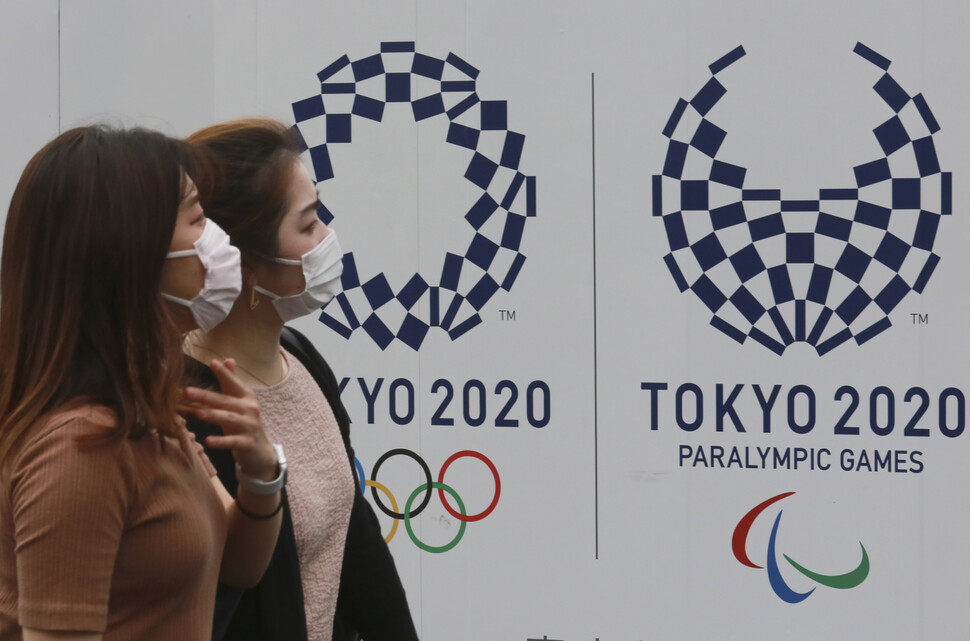 16일 일본 도쿄에서 시민들이 도쿄올림픽 포스터 앞을 마스크를 쓴 채 지나가고 있다. 도쿄/AP 연합뉴스