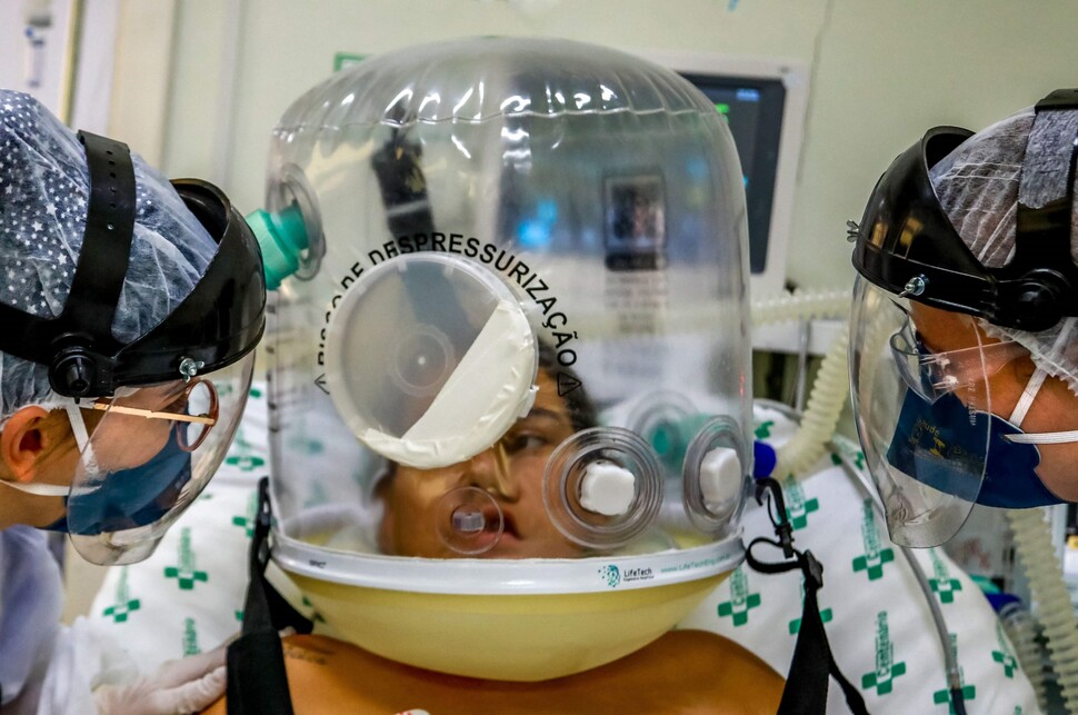 코로나19에 감염돼 호흡 기능이 떨어진 환자(가운데)가 2021년 4월16일(현지시각) 브라질 남부 히우그란지두술주 센테나리우병원에서 관을 삽입하지 않고 호흡을 도와주는 새 장비를 쓴 채 의료진과 대화하고 있다.