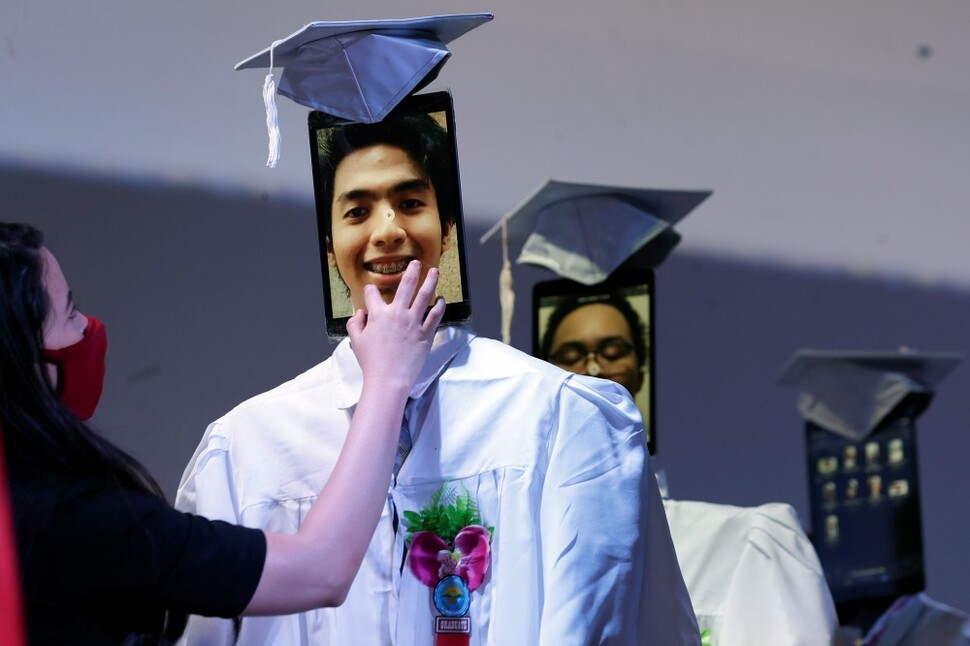 필리핀 마닐라 타기그의 한 학교에서 5월22일 ‘사이버 졸업식’이 열리고 있다. 페이스북으로 생중계된 온라인 졸업식에서 한 교사가 졸업가운 위에 세운 태블릿피시에 학생 얼굴을 띄우고 있다.