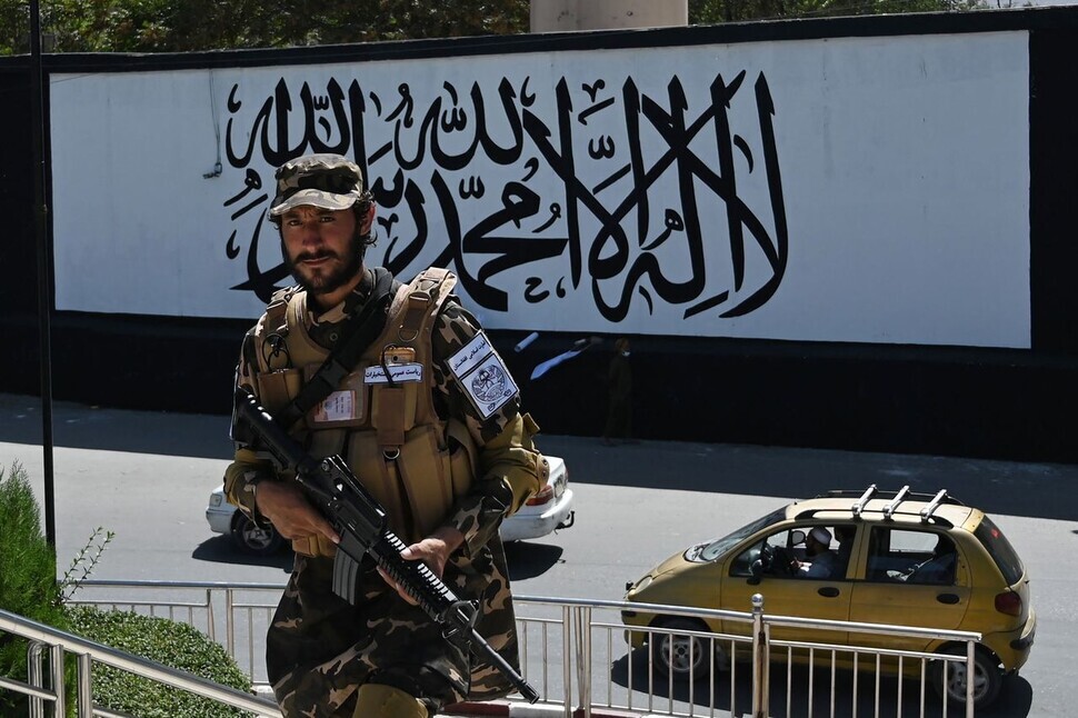 A member of the Taliban stands guard outside the US embassy compound in Kabul, Afghanistan, Wednesday, in front of a wall painted with the Taliban’s flag. At the end of August, US forces and embassy employees were withdrawn from Afghanistan. (AFP/Yonhap News)