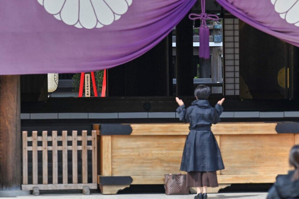A woman claps her hands before Yasukuni Shrine, where Class-A war criminals are enshrined, on April 21. On the left-hand side, red ribbons of the “masakaki” ritual offering from Japanese Prime Minister Fumio Kishida are visible. (Yonhap News)