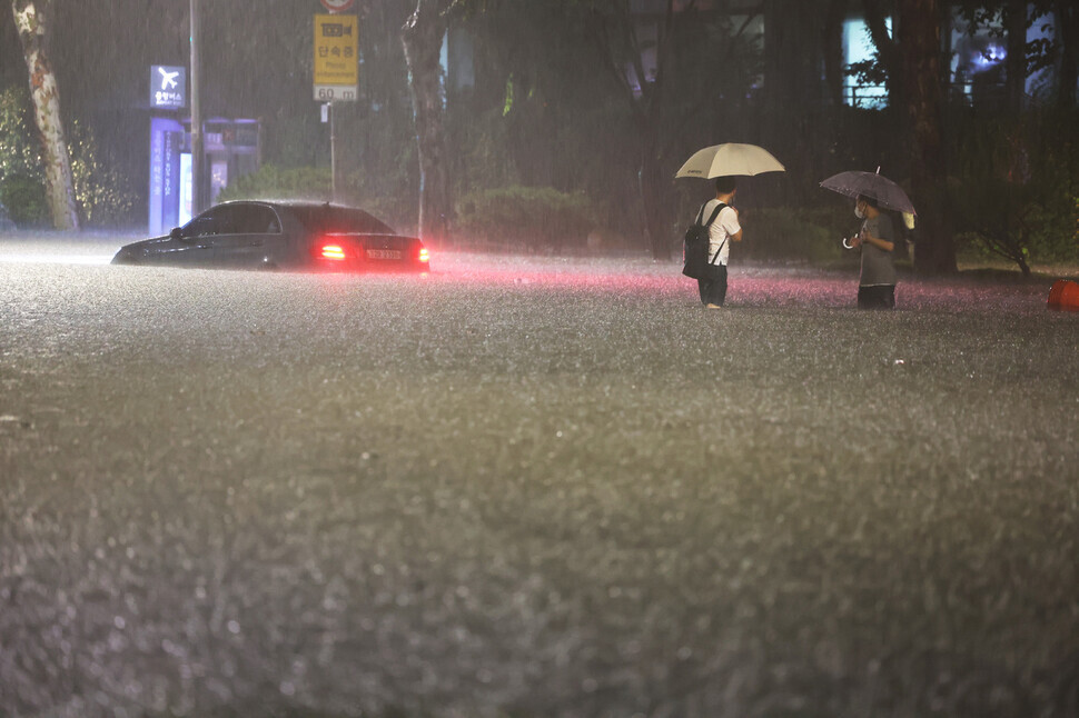A car sits on a flooded road near Daechi Station in Gangnam, Seoul, on Aug. 8 as two people standing in the flood water look on. (Yonhap News)