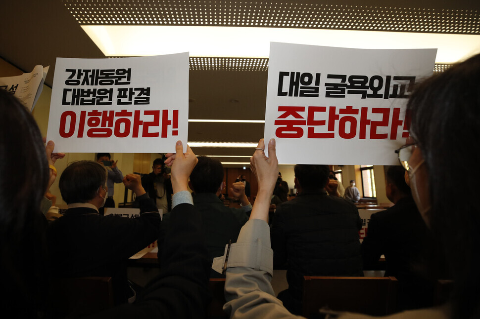 Participants in the press conference hold up signs reading “Implement the Supreme Court ruling on forced mobilization!” and “Put a stop to submissive diplomacy to Japan!” (Kim Hye-yun/The Hankyoreh)