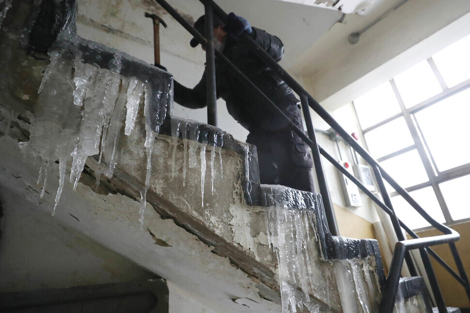 A resident at a flophouse in the Dongja neighborhood of Seoul’s Yongsan District attempts to break up the ice covering the stairs in his building with a hammer on Jan. 26. (Kang Chang-kwang/The Hankyoreh)