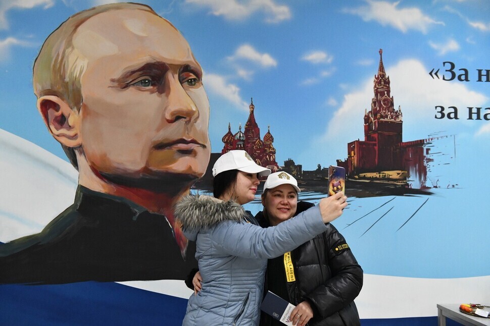 Two locals snap a photo in front of a mural of Russian President Vladimir Putin in Donetsk, Russian-occupied Ukraine, after voting in the presidential election on March 15, 2024. (EPA/Yonhap)