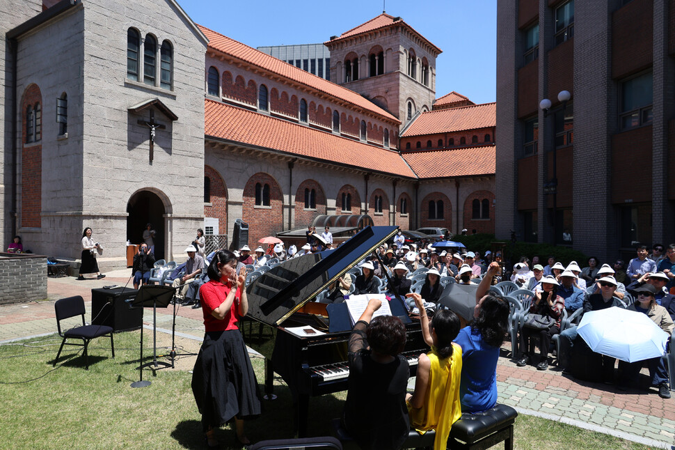 최은경(맨 앞 앉은 이 왼쪽부터), 강은하, 오정선 연주자가 2025년 6월4일 서울 중구 정동 대한성공회 서울대성당 마당에서 하나의 피아노로 ‘세비야의 이발사 서곡' 연주를 마치며 손을 들어 올리고 있다.