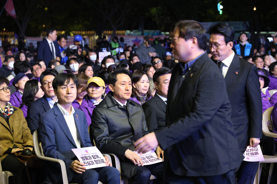 김민석 국무총리(오른쪽 선 이)가 유가족협의회 관계자(왼쪽 선 이)의 안내를 받아 외국인 유가족을 만나러 가는 동안 오세훈 서울시장(앞줄 왼쪽 셋째)이 자리에 앉아 있다.