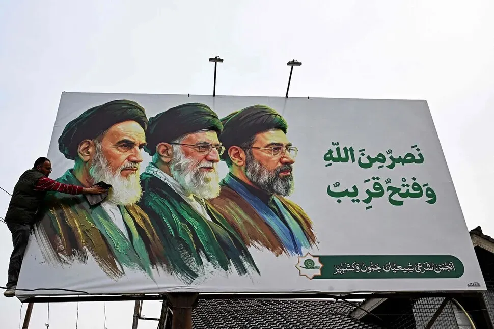 A man cleans a billboard in Iran showing the country’s supreme leaders since 1979, from Ayatollah Ruhollah Khomeini (left) to Ayatollah Ali Khamenei (center), and his son, the new supreme leader, Mojtaba Khamenei (right), on March 23, 2026. (AFP/Yonhap)