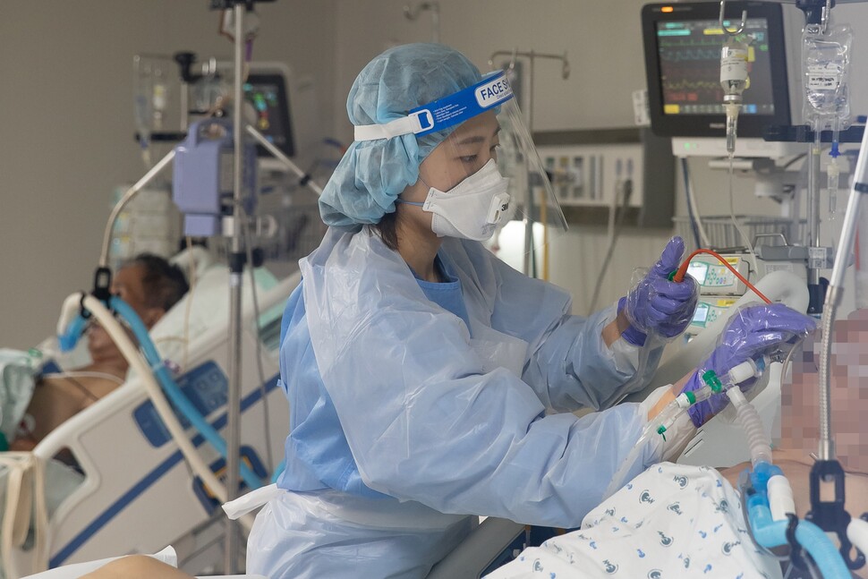 간호사가 중증환자에게 연결한 튜브를 살펴보고 있다.