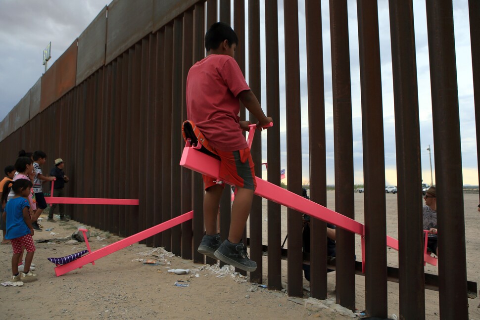 2019년 7월, 미국과 멕시코를 가르는 거대한 철제 장벽에 만들어진 설치예술인 분홍색 시소에서 멕시코 어린이(왼쪽)와 미국 쪽 관광객이 시소를 타고 있다. AFP 연합뉴스