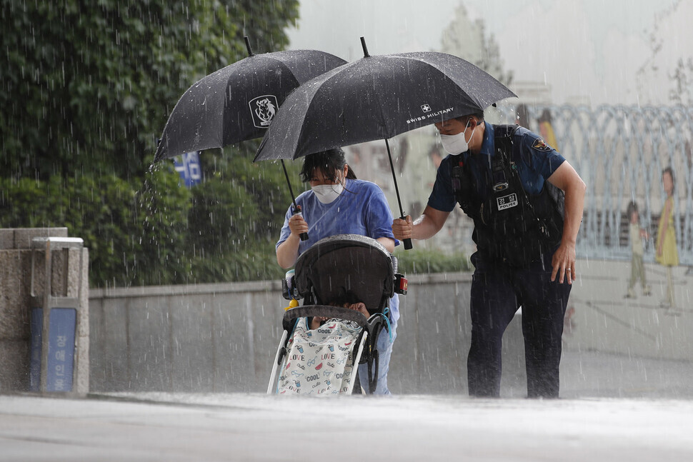 Assistant Inspector Byun Young-woo holds an umbrella for a mother and a child while escorting them to a place where they could take shelter from the rain on Wednesday. (Lee Jeong-a/The Hankyoreh)