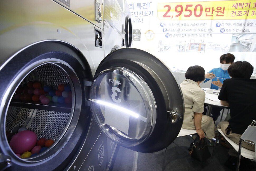 Visitors at the International Franchise Show held at Coex in Seoul receive a quote from a representative at the booth for a self-service laundromat chain on Thursday. (Lee Jeong-a/The Hankyoreh)