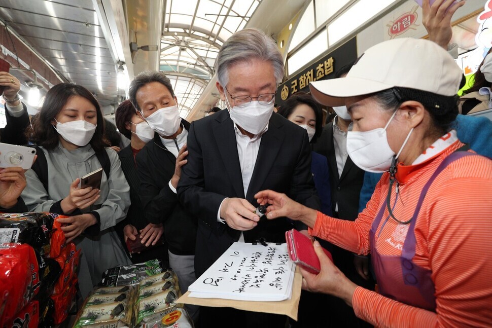 Democratic Party nominee for president, Lee Jae-myung, signs the guestbook of a vendor during a visit to Sinwon Market in Seoul’s Gwanak District on Wednesday morning. (Kim Bong-gyu/The Hankyoreh)