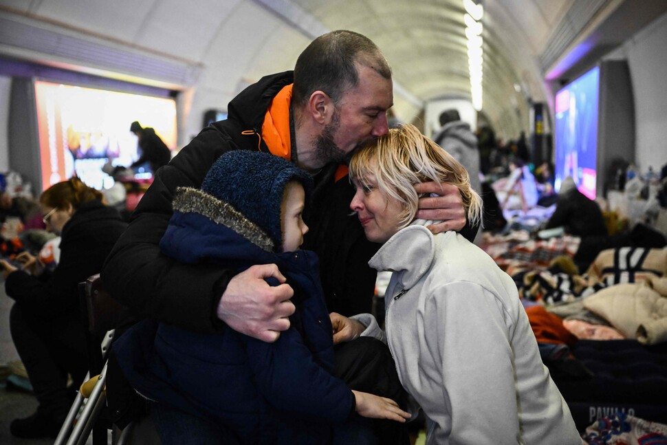 우크라이나 주요 도시에 대한 러시아의 폭격이 계속된 2022년 3월2일(현지시각) 공습 대피소로 사용하는 키이우의 지하철역에서 세르히 바딜레비치(41·가운데)가 아이를 끌어안은 채 아내 나탈리아의 머리에 입 맞추고 있다. 이들 뒤편에 지하에서 밤을 보내려는 시민들이 이부자리를 편 채 쉬고 있다.