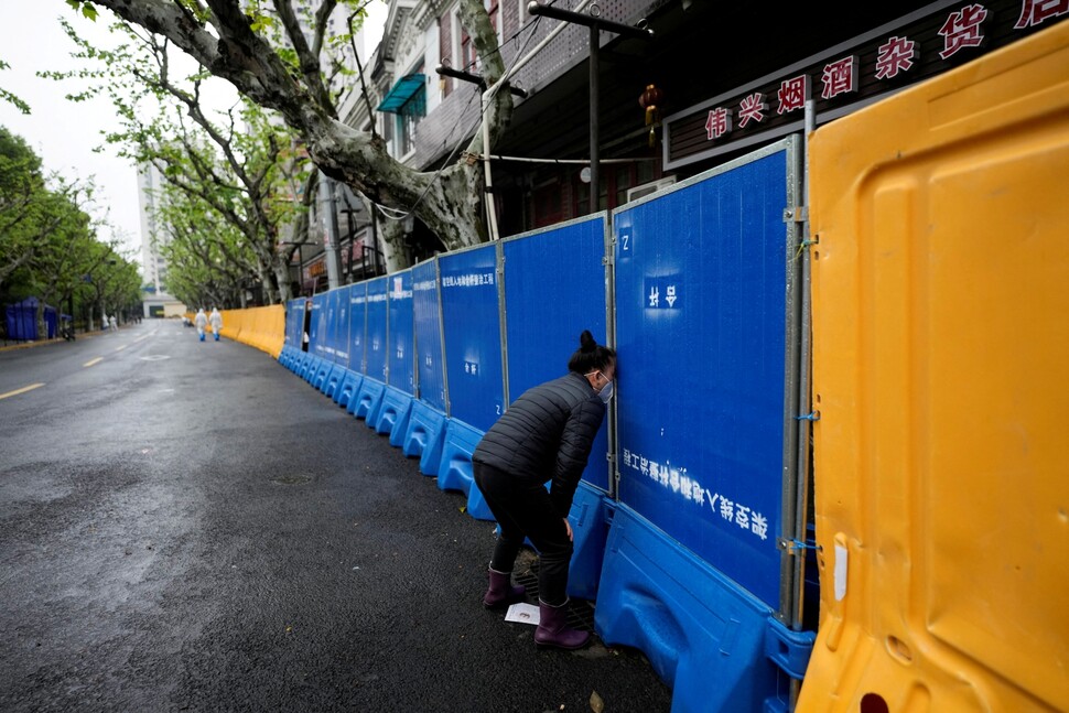 2022년 4월14일 코로나19로 인한 중국 상하이 봉쇄 중 한 여성이 식품을 사려고 바리케이드 틈을 들여다보고 있다. REUTERS