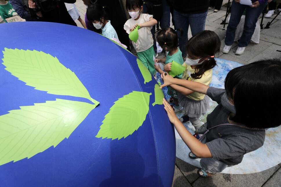 Children participating in the constitutional complaint stick green leaves to a model of the Earth outside the Constitutional Court of Korea on June 13. (Kim Myoung-jin/The Hankyoreh)