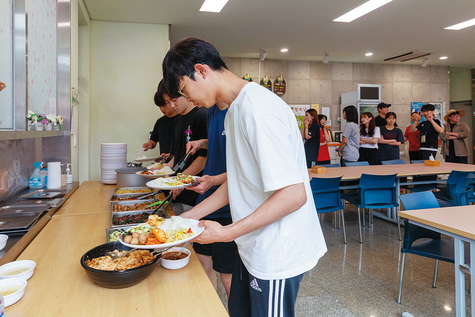 오전 밭일을 끝낸 학생들이 아침을 먹기 위해 마을회관에 마련된 식당에 줄을 서서 큰 접시에 밥과 반찬을 담고 있다.