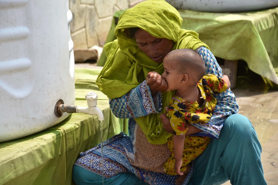 2022년 9월13일 홍수 피해 지역인 파키스탄 남부 신드주 라르카나에서 한 수재민이 아이에게 손으로 물을 받아 먹이고 있다. EPA 연합뉴스