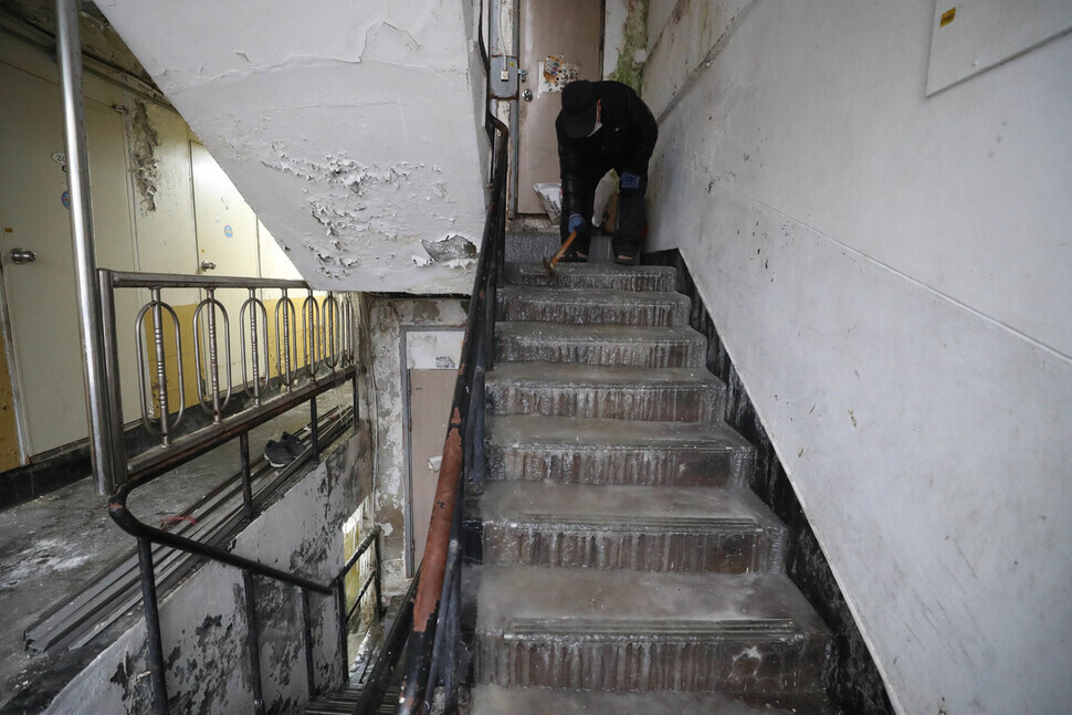 A resident at a flophouse in the Dongja neighborhood of Seoul’s Yongsan District attempts to break up the ice covering the stairs in his building with a hammer on Jan. 26. (Kang Chang-kwang/The Hankyoreh)