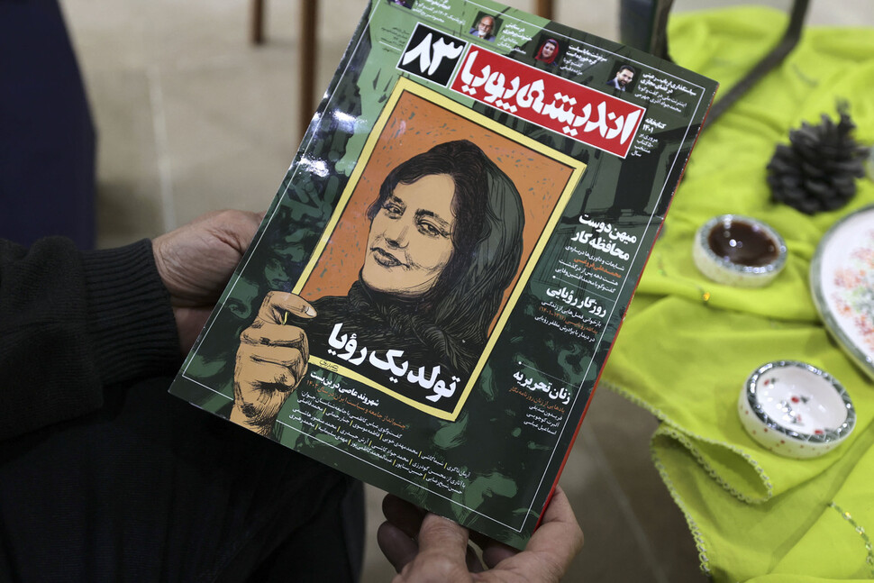 14일(현지시각) 이란 테헤란에서 한 시민이 마흐사 아미니의 얼굴이 그려진 이란 잡지를 들고 있다. 평범한 이란 여성이었던 아미니는 지난해 9월 히잡 착용 미비로 도덕경찰에 붙잡혔다 숨지면서 이란 전역에서 자유와 저항을 상징하는 인물이 됐다. 테헤란/AFP 연합뉴스
