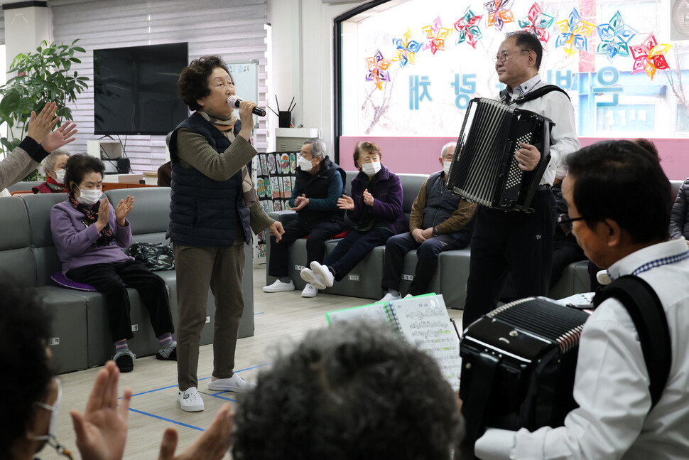 김인자(왼쪽 선 이)씨가 2024년 2월23일 경기 고양시 덕양구 행신동 은빛사랑채에서 정희준(오른쪽 선 이) 단장과 단원들의 반주에 맞춰 &lt;여자의 일생&gt;을 노래하고 있다.
