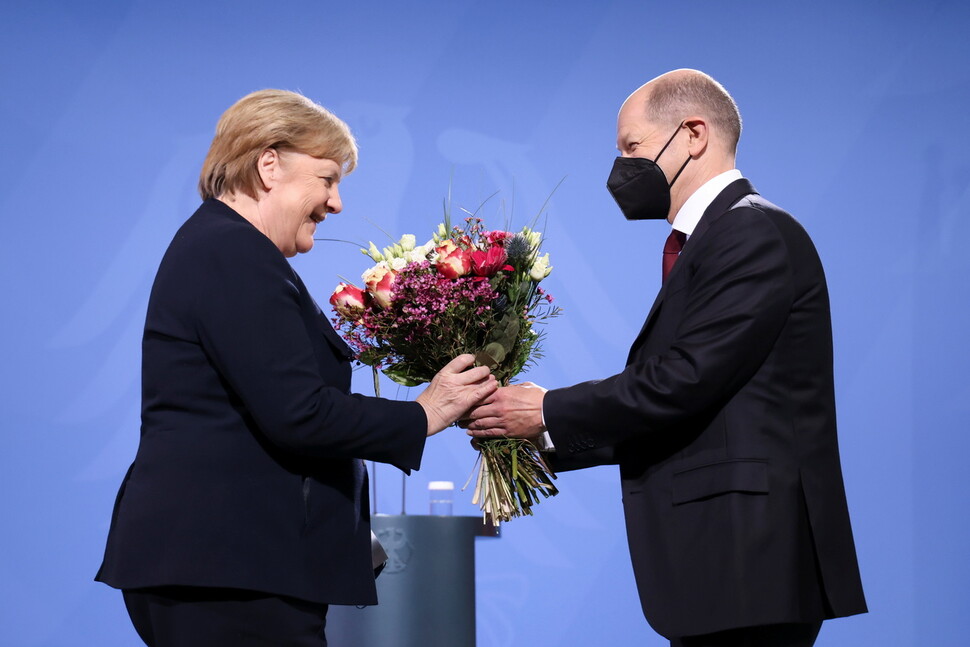 2021년 12월8일 독일 베를린의 총리실에서 사회민주당의 올라프 숄츠 새 총리(왼쪽)가 전임자인 기민련의 앙겔라 메르켈 전 총리에게 꽃다발을 선물하고 있다. 두 사람은 메르켈 총리의 마지막 임기 때 연정을 구성해 함께 독일을 이끌었다. REUTERS