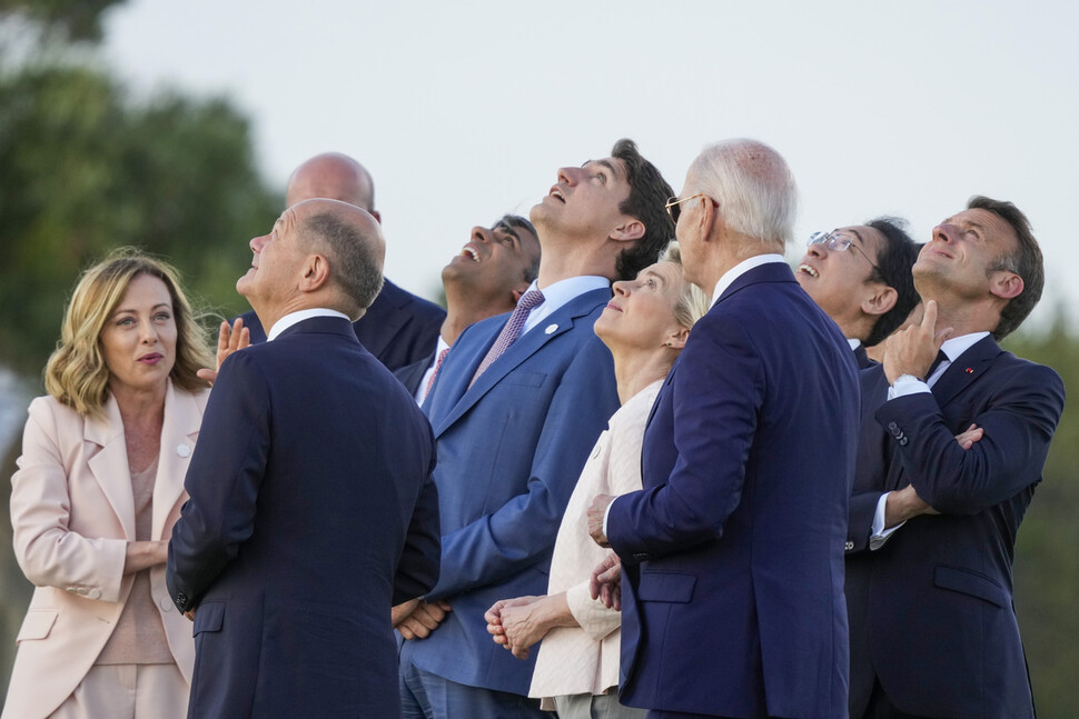 2024년 6월13일 이탈리아 남동부 풀리아주에서 열린 주요 7개국(G7) 정상회의 개막 행사에 참석한 정상들이 고개를 들어 공중낙하 공연을 지켜보는 가운데 조르자 멜로니 이탈리아 총리(맨 왼쪽)가 곁에 선 올라프 숄츠 독일 총리에게 뭔가 말하고 있다. AP 연합뉴스