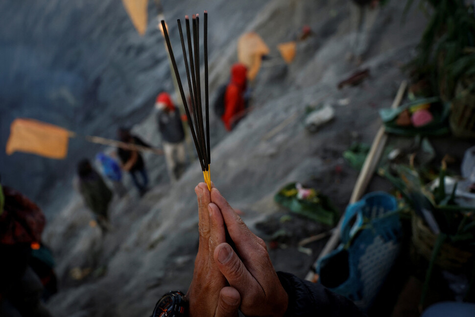 텡게르족 힌두교 신자가 브로모 화산에 공물을 던지기 전에 향을 들고 기도하고 있다.