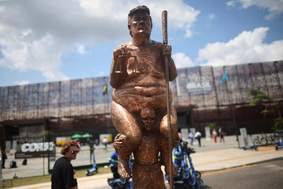 20일(현지시각) 브라질 벨렝 기후총회 행사장 앞에 소년의 어깨 위에 올라탄 도널드 트럼프 미국 대통령을 형상화한 조형물이 설치돼 있다. 벨렝/로이터 연합뉴스