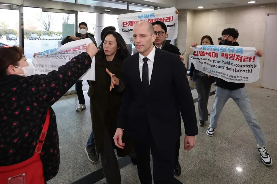 Unionists hold up signs regarding accountability for a customer data leak and demands about a collective bargaining agreement as Harold Rogers, the new interim CEO of e-commerce giant Coupang, arrives at the National Assembly on Dec. 17, 2025, for a hearing on the company’s data breach. (Choi Hyeon-su/Hankyoreh)