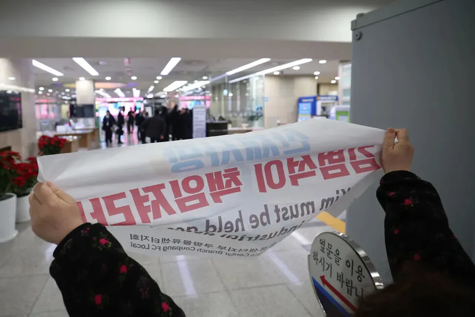 Unionists hold up signs regarding accountability for a customer data leak and demands about a collective bargaining agreement as Harold Rogers, the new interim CEO of e-commerce giant Coupang, arrives at the National Assembly on Dec. 17, 2025, for a hearing on the company’s data breach. (Choi Hyeon-su/Hankyoreh)
