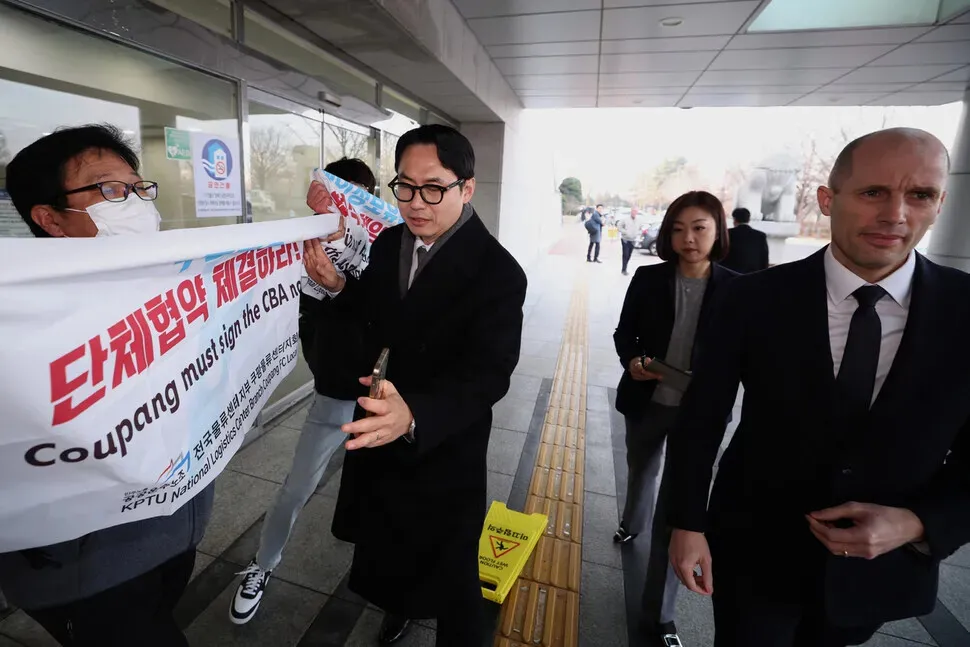 Unionists hold up signs regarding accountability for a customer data leak and demands about a collective bargaining agreement as Harold Rogers, the new interim CEO of e-commerce giant Coupang, arrives at the National Assembly on Dec. 17, 2025, for a hearing on the company’s data breach. (Choi Hyeon-su/Hankyoreh)