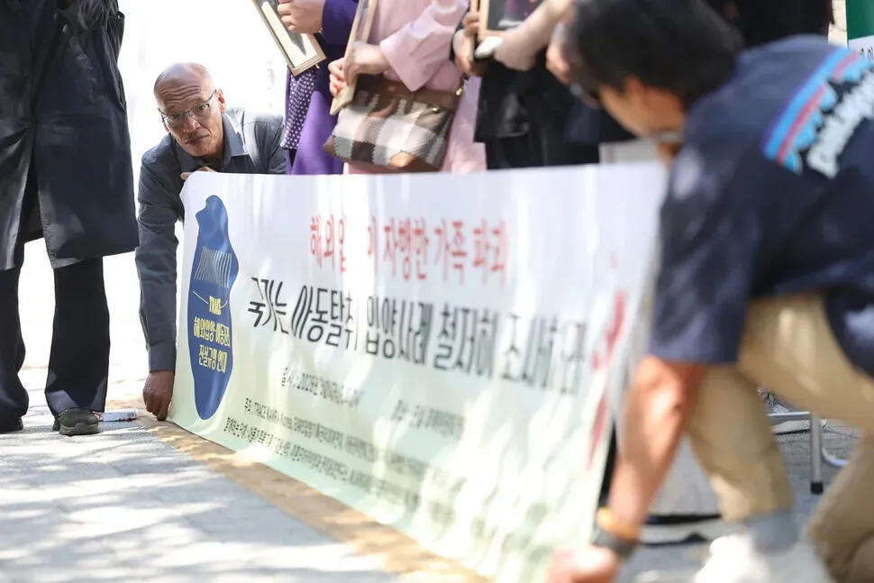 Simon Hokwerda holds a banner during a press conference by TRACE, a coalition of adoptee groups, held outside the Truth and Reconciliation Commission in Seoul on May 8, 2026. (Kim Young-won/Hankyoreh)