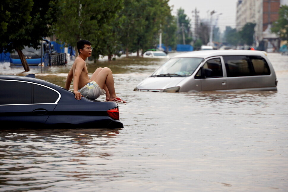 A man sits on a stranded vehicle on a flooded road following heavy rainfall in Zhengzhou, Henan province, China, on July 22. (Reuters/Yonhap News)