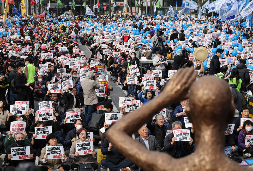 Participants in a nationwide rally on March 11 condemning Seoul’s “degrading” solution to forced mobilization compensation and calling for apology and compensation by Japan hold up signs as they sit in front of a statue in Seoul Plaza representing victims of forced labor. (Kim Hye-yun/The Hankyoreh)