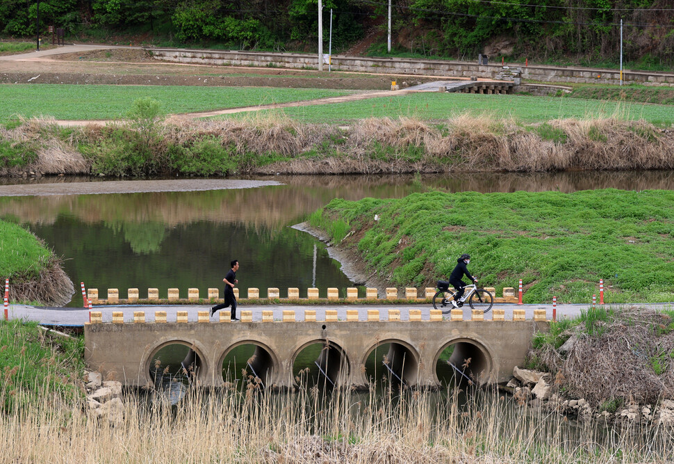 현대식으로 지은 강매세월교 위로 시민들이 달리거나 자전거를 탄 채 건너고 있다. 위쪽에 강매석교가 보인다.