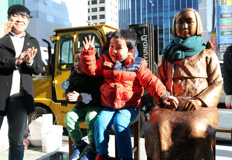 A child takes poses for a photo next to the comfort woman statue in front of the Japanese consulate in Busan