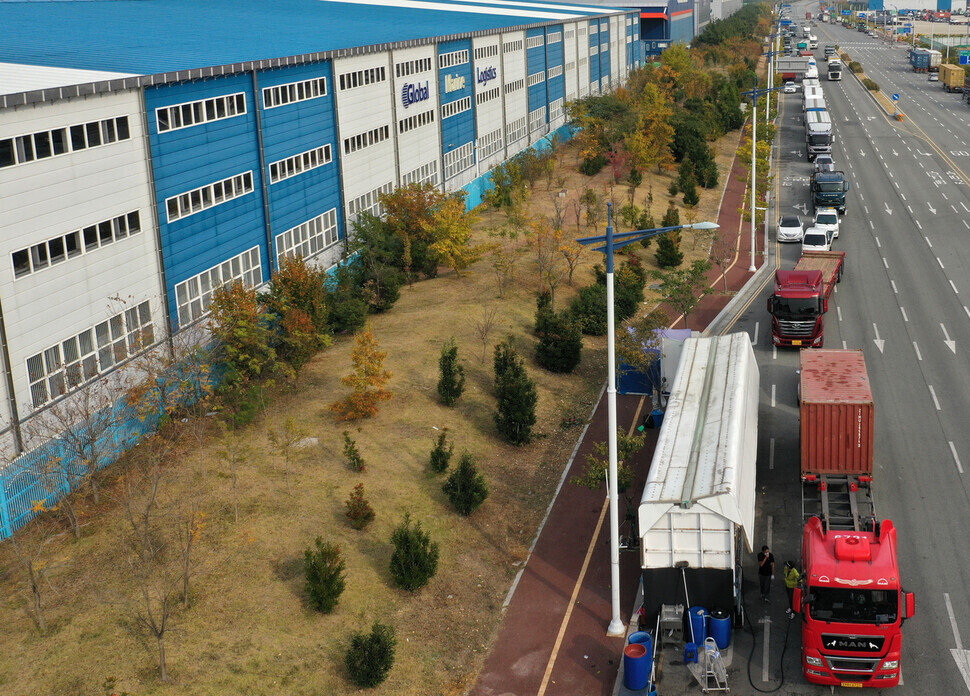 As the shortage of urea water solution continues, cargo trucks form a long line as they wait to buy the fluid being sold along the street in the city of Changwon’s Jinhae District, near the Busan New Port Hinterland Complex, on Friday. (Yonhap News)