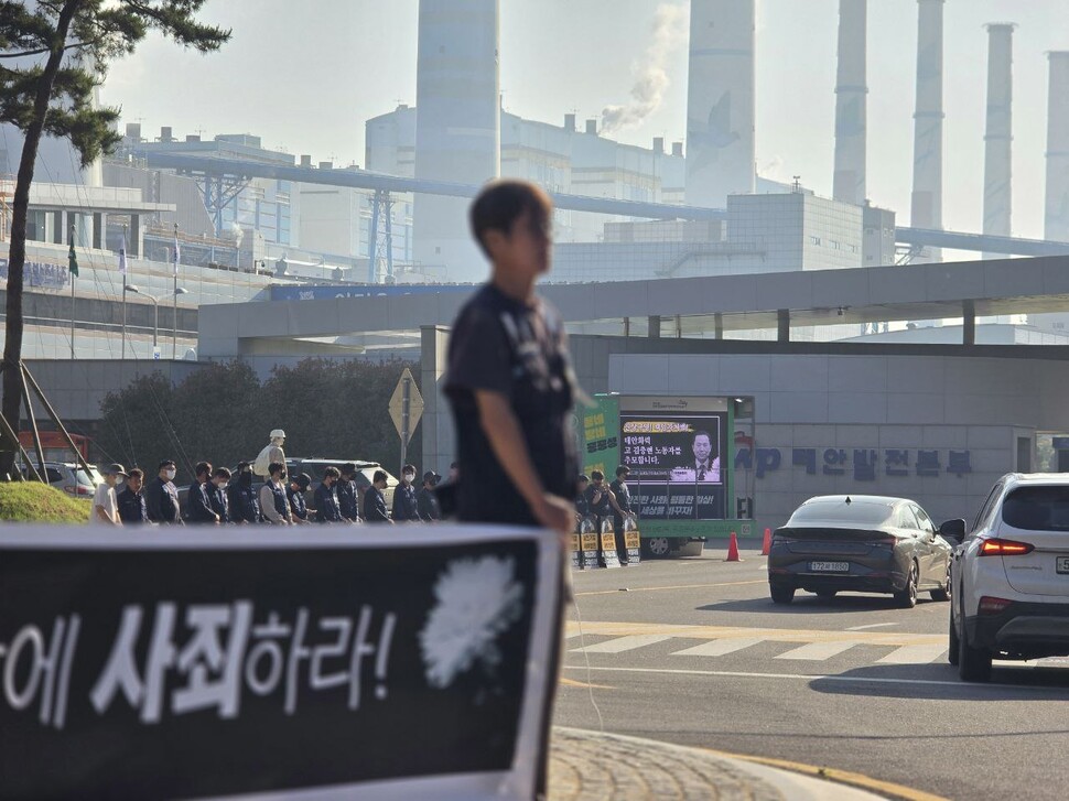 2025년 6월8일 충남 태안화력발전 앞에서 활동가들이 김충현씨의 죽음에 사죄하라고 요구하는 펼침막을 들고 있다. 멀리 김충현씨 영정이 차량 전광판에 띄워져 있다. 태안화력김충현대책위 제공