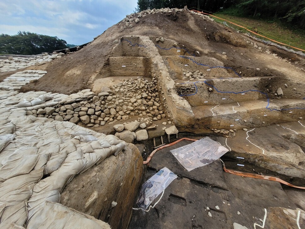 The wall running through the remains in the center is Wolseong Palace’s western wall. An endeavor to widen the wall can be seen, with stones stacked on one side, and covered in a layer of mud on the other. Two large pieces of paper on the basal bed below it show where remains of a woman were recently found, as well as the two remains found in 2017. (Roh Hyung-suk/The Hankyoreh)