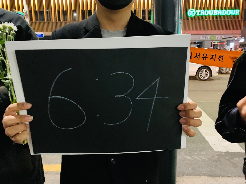 A young person in black clothing is holding a placard that says “6:34” near Itaewon Station, Seoul, on Friday, Nov. 4. The demonstration was held to commemorate the victims of the Itaewon crowd crush and to demand that the South Korean government be held responsible for the disaster. (Photo provided by John R. Eperjesi)
