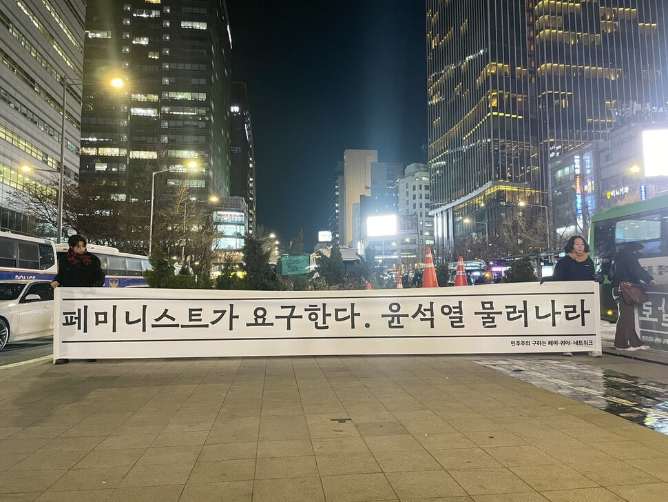 ‘민주주의 구하는 페미-퀴어-네트워크’ 소속 활동가들이 2024년 12월4일 서울 종로구 동화면세점 앞 횡단보도에서 윤석열 대통령의 퇴진을 요구하는 펼침막을 들고 서 있다. 한국여성의전화 제공