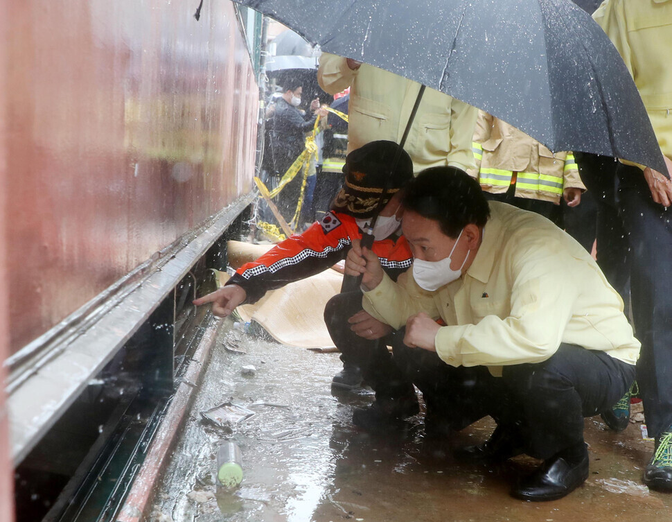While surveying flood damage on Aug. 9, President Yoon Suk-yeol peers into the semi-basement dwelling in Seoul’s Gwanak District where three family members died during flooding. (Yonhap News)