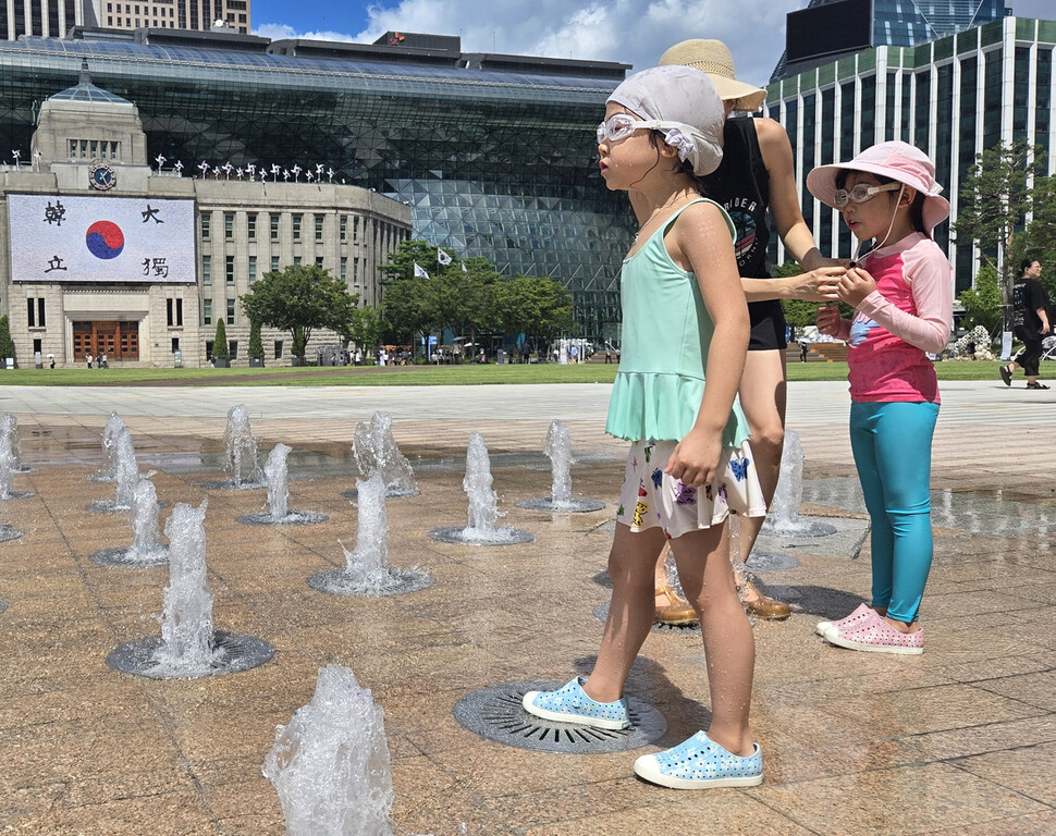 서울광장 분수 주위에서 한 엄마가 아이들에게 물안경과 모자를 씌우고 있다.